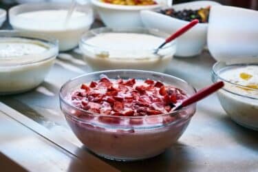 Frascos de probióticos junto a frutas frescas y un vaso de yogur natural.